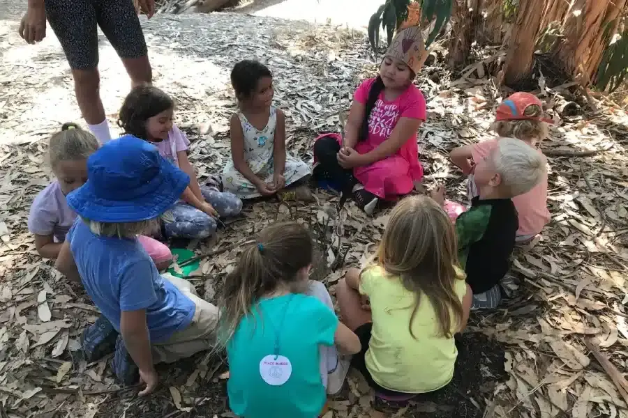 Children sitting in a nature circle during a homeschool outdoor enrichment program, engaged in storytelling under eucalyptus trees.