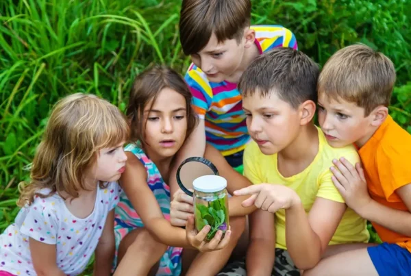 children exploring nature with magnifying glass examining plants and insects in outdoor learning environment