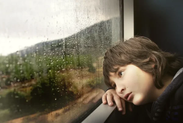 Child looking bored while staring out a rain-covered window, reflecting the value of quiet, unstructured moments for imagination and creativity.