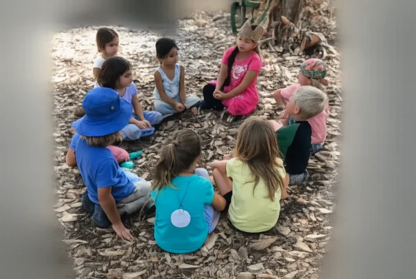 nature-based-play-main-blog-image Children sit in a circle outdoors during a Nature Scouts Collective group activity centered on nature-based play, learning and exploration.